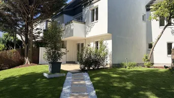 Gepflegter Gartenbereich mit Rasenfläche und Steinweg, der zum modernen Gebäude mit Terrasse führt.