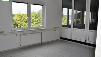 Helles Büro mit großen Fenstern, die einen Blick ins Grüne bieten, und einem Fliesenboden.