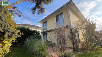 Hausfassade mit sonniger Terrasse, umgeben von einem gepflegten Garten und viel Grün.