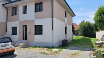 Neubau-Doppelhaushälfte mit beiger und weißer Fassade und kleinem Vorgarten.