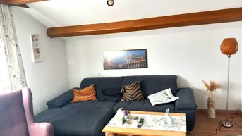 Gemütliches Wohnzimmer mit Holzbalken an der Decke und bequemer Sofalandschaft.