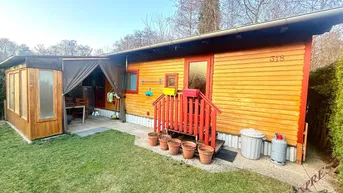 Kleines Holzhaus mit Gartenbereich und überdachter Terrasse, ideal für entspannte Stunden im Freien.