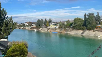 Blick über einen ruhigen Kanal mit Häusern am gegenüberliegenden Ufer unter blauem Himmel.