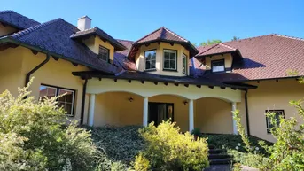 Großzügiges Einfamilienhaus mit traditioneller Architektur, Walmdach und gepflegtem Vorgarten unter blauem Himmel.