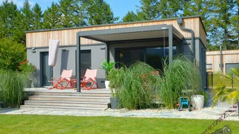Moderne Hausfassade mit Holzverkleidung, großer Terrasse und Gartenbereich.