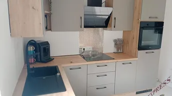 Moderne L-förmige Küche mit grauen Schränken, Holzarbeitsplatte und integrierten Geräten.