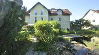 Haus mit großem Garten, üppiger Vegetation und einem Naturteich mit kleinem Steg.