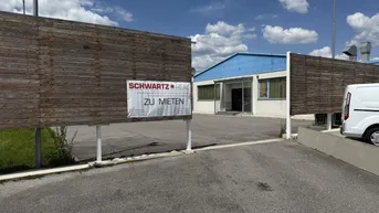 Einfahrt zu einem Gewerbeobjekt mit einem "Zu vermieten"-Schild an einer Holzumzäunung unter blauem Himmel.