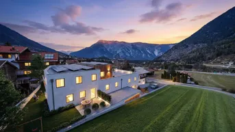 Moderne Wohnanlage mit großem Garten, Terrasse und Bergblick bei Sonnenuntergang.