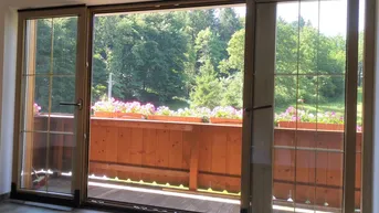 Heller Balkon mit Holzboden, Blumenkästen und weitem Blick ins Grüne.