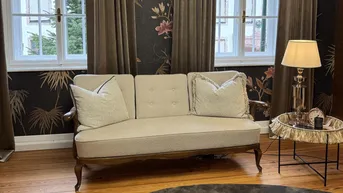 Gemütliches Wohnzimmer mit elegantem Sofa, dunkler Tapete und Holzboden, bietet einen grünen Ausblick.
