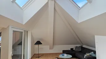 Helles Wohnzimmer im Dachgeschoss mit großen Dachfenstern und Zugang zum Balkon.