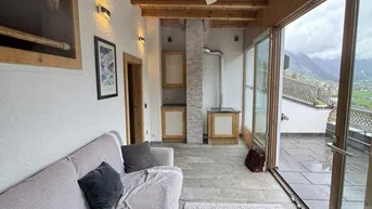 Gemütliches Wohnzimmer mit Holzbalkendecke, Kaminofen und Zugang zu einer großen Terrasse mit Bergblick.