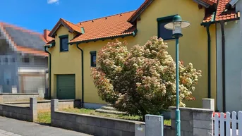 Gelbes Einfamilienhaus mit rotem Ziegeldach und Vorgarten an einem sonnigen Tag.