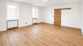 Heller, leerer Raum mit Laminatboden, weißen Wänden und moderner Schiebetür.