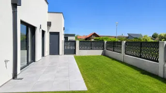 Moderne Terrasse mit hellen Fliesen und angrenzendem Rasenbereich eines Neubaus.