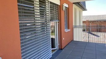 Heller Balkon mit Fliesenboden, Metallgeländer und Blick auf umliegende Gebäude.