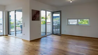 Helles Wohnzimmer mit Holzboden und Zugang zu einem Balkon, bietet einen weiten Blick.