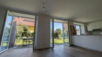 Heller Wohnbereich mit großen Glasfronten, die direkten Zugang zum Garten bieten.