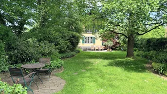 Grüner Garten mit Rasenfläche, Bäumen und zwei gemütlichen Sitzbereichen im Freien.