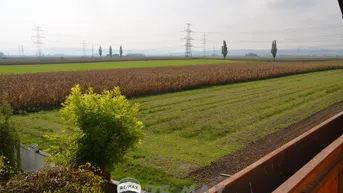 Weitläufiger Blick über Felder und ländliche Landschaft mit Strommasten am Horizont.
