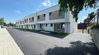 Moderne Reihenhäuser mit weißer Fassade und braunen Akzenten unter blauem Himmel.
