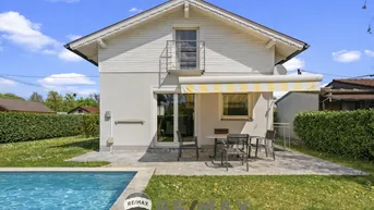 Rückansicht des Hauses mit privatem Pool, Terrasse und Gartenbereich unter blauem Himmel.