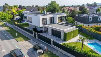 Moderne Villa mit Flachdach, großem Pool und Doppelgarage in grüner Umgebung.
