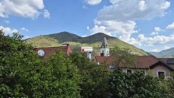 Weitblick über Dächer und grüne Hügel mit einem Kirchturm in der Ferne.