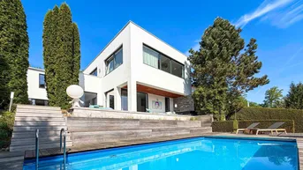 Moderne Villa mit weißer Fassade, großem Pool und Holzterrasse unter blauem Himmel.