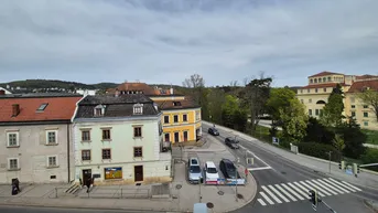 Stadtansicht mit historischen Gebäuden, einer belebten Straße und einem Zebrastreifen.