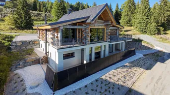 Modernes Blockhaus mit traditionellen Holzelementen und großen Fensterfronten in alpiner Umgebung.