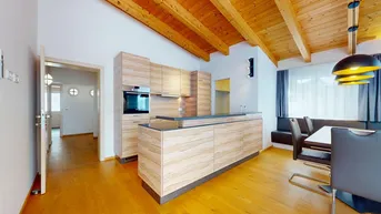 Offener Wohn- und Essbereich mit moderner Holzküche, Kücheninsel und sichtbaren Holzdeckenbalken.