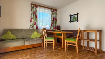 Gemütlicher Wohn- und Essbereich mit Holzboden, bequemer Couch und Blick ins Grüne.