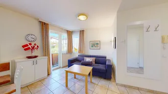 Gemütlicher Wohnbereich mit blauer Couch und Spiegel, bietet Zugang zum sonnigen Balkon.