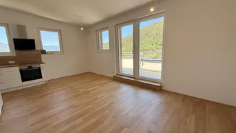 Heller Wohnbereich mit Holzboden und Zugang zu einem Balkon, bietet einen schönen Blick auf die Berge.