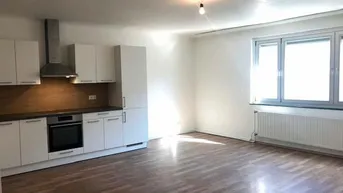 Heller offener Wohnbereich mit moderner Einbauküche, Laminatboden und großem Fenster.