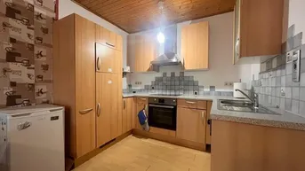 Funktionale Küche mit hellen Holzschränken, grauer Arbeitsplatte und gefliestem Spritzschutz.