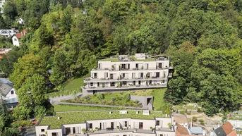 Luftaufnahme moderner Apartmentgebäude in Hanglage, umgeben von üppiger grüner Natur und Bäumen.