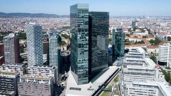 Luftaufnahme eines modernen Bürokomplexes mit Glasfassaden in einer städtischen Umgebung und umliegenden Gebäuden.