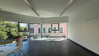 Geräumiges, leeres Büro mit großen Fenstern, die einen Blick auf die Straße und ein historisches Gebäude bieten.