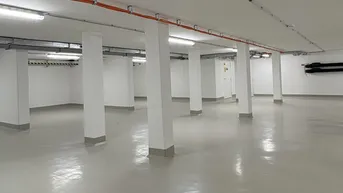 Großer, leerer Raum im Untergeschoss mit vielen Säulen, hellgrauem Boden und sichtbaren Installationen an der Decke.