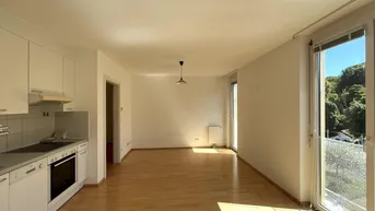 Helles, offenes Wohnzimmer mit integrierter Küche, Parkettboden und Zugang zum Balkon.