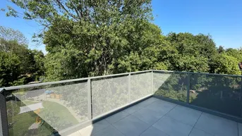 Geräumiger Balkon mit modernem Metallgeländer und Blick ins Grüne unter blauem Himmel.