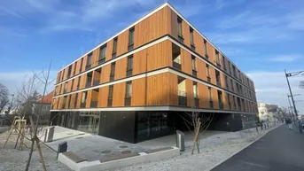 Modernes Mehrfamilienhaus mit Holzfassade und großen Fenstern, umgeben von neu angelegten Außenbereichen.