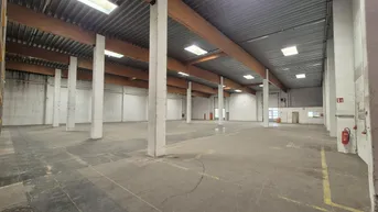 Geräumige Lagerhalle mit hoher Decke, Holzbalken und Oberlichtern, ideal für industrielle Nutzung.