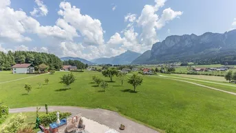 Weitläufiger Blick über grüne Wiesen und Berge mit einer Terrasse und Whirlpool im Vordergrund.