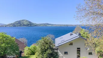 Modernes Haus mit Satteldach und großen Fenstern, eingebettet in eine grüne Landschaft mit Seeblick.