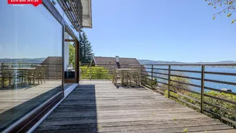 Geräumige Holzterrasse mit Esstisch und atemberaubendem Blick auf den See und die umliegende Landschaft.