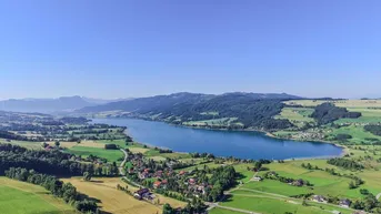 Panoramablick auf den See, umgeben von grünen Hügeln und einem malerischen Dorf.